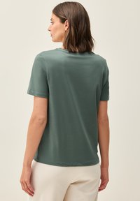 T-shirt à manches courtes et col rond en tissu vert clair avec une coupe décontractée. Présente des coutures simples et une texture lisse.