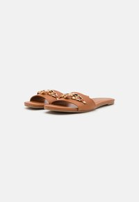 Öppen tå slide-sandaler i tan syntetiskt material, med en guldkedja som accent över ovansidan och en platt trä-sula.