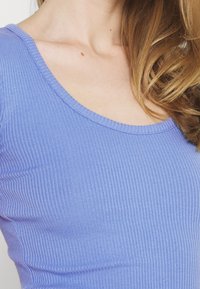 Light purple ribbed long-sleeve top with a wide scoop neckline. The fabric has a soft texture and prominent vertical lines.