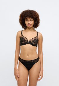 Μαύρο κορμάκι με δαντέλα και ενίσχυση, με διάφανες θήκες που κοσμούνται με λουλούδια και ρυθμιζόμενα λουράκια. Συμπεριλαμβάνονται μαύρο διάφανο εσώρουχο αντίστοιχου σχεδίου.