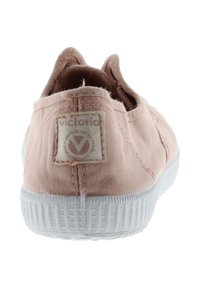 Zapatillas de lona rosas tipo slip-on con suela de goma blanca; cuentan con un parche de logo rectangular en la parte trasera y detalles de costura a lo largo de los bordes.