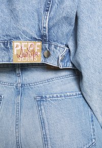 Jasnoniebieski zestaw z kurtką dżinsową i jeansami z widoczną metką "Pepe Jeans" oraz metalowym guzikiem na dolnej części pleców kurtki.