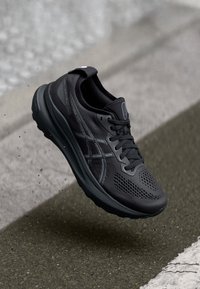 Black running shoe with mesh upper, textured accents, and a thick outsole. Features the ASICS logo and breathable perforations on the sides.