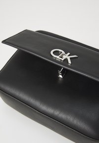 Borsa a mano nera in pelle con una texture liscia, dotata di una chiusura a scatto in argento con logo CK e una forma rettangolare strutturata.