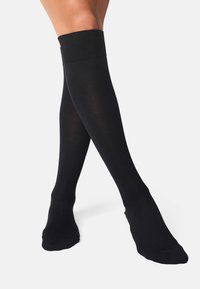 Medias negras hasta la rodilla hechas de una tela suave y elástica con un puño acanalado y un diseño liso y sin costuras.