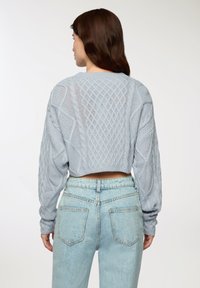 Maglione lavorato a maglia di un azzurro chiaro con un design cropped e intricate trame a cavo. Maniche lunghe e scollatura rotonda. Abbinato a un jeans a vita alta.