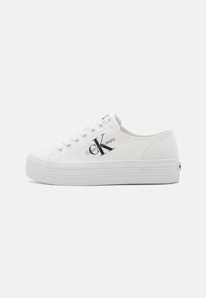 Hvide lave platform sneakers med Calvin Klein Jeans-logo i sort på siden og hvide snørebånd.