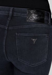 Jeans in denim scuro con un'etichetta nera lucida, tasca posteriore con un logo triangolare argentato e dettagli di cucitura sottili.