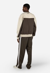 Hnědé a krémové oversized sweatshirt s kontrastním barevným blokem. Spárované s tmavě hnědými kalhotami s bílými bočními pruhy a měkkou texturou.