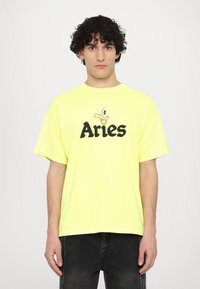 T-shirt oversize di cotone giallo brillante con testo nero "Aries" e grafica di un'anatra in stile cartoon. Vestibilità comoda e maniche corte.