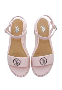 Světle růžové sandály se širokými pásky, kulatým kovovým emblémem a polstrovanou hnědou vnitřní podrážkou. Nastavitelný pásek kolem kotníku pro bezpečné uchycení.