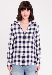 Chemise à manches longues et col en V à carreaux, avec un motif à damier bleu marine et blanc, devant à boutons et en tissu doux. Associée avec un jean bleu clair.