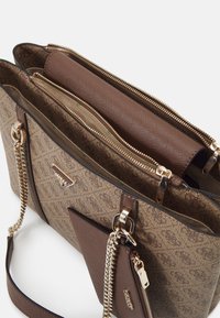 Sac fourre-tout en cuir marron avec des poignées en chaîne dorée, poche zippée à l'avant et deux compartiments principaux zippés, présentant un motif de tissu texturé.