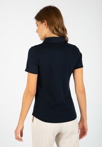 Polo shirt blu navy a maniche corte, con colletto e texture a costine. Modello mostrato di spalle con capelli morbidi e fluenti.