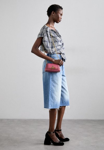 Ternet bluse, blå denim culottes med frynset kant, rød håndtaske med dekorativt hardware og sorte ankelsandaler.