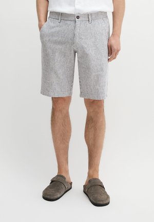 Man draagt grijze en witte verticale gestreepte korte broek en grijze instapschoenen tegen een effen lichte achtergrond.