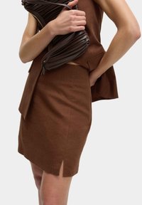 Top sans manches en lin marron et jupe ajustée assortie avec une fente sur le côté, accompagnés d'une pochette texturée marron avec fermeture éclair.