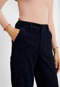 Navyblå manchesterbyxor med vertikal ribbad struktur, utrustade med sidofickor och elastisk midja. Mjuk tyg; inga synliga mönster eller detaljer.