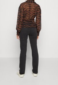 Camicia trasparente a righe marroni e nere con maniche lunghe, abbinata a jeans neri e sneakers bianche, vista da dietro.
