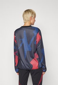 Langermet skjorte i svart med et geometrisk mønster i rødt og blått. Myk, teksturert stoff; har rund hals og avslappet passform.