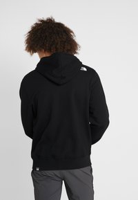 Zwarte hoodie met een effen ontwerp, voorzien van een trekkoordkap, geribbelde manchetten en een klein wit logo op de linkerschouder aan de achterkant.