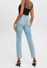 Jean en denim bleu clair avec une coupe droite, cinq poches et une étiquette beige à l'arrière. Associé à un top court noir et des sandales à talons.