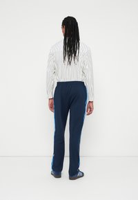 Navy Sweatpants mit blauen Seitenstreifen, elastischem Bund und einer lockeren Passform. Kombiniert mit einem weißen gestreiften Langarmshirt.