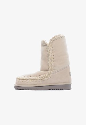 Beige suède winterlaarzen tot halverwege het kuit met dikke gevlochten stiksels langs de randen en een platte rubberen zool.