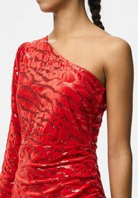 Raudona blizgučių suknelė su viena petneša, pasižyminti tekstūriniu, aksominiu audiniu ir prigludusia, raukšlėta siluetu.