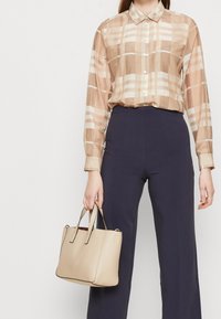 Beige ternet bluse med lange ærmer og krave, parret med navy høj talje bukser. Beige tekstureret håndtaske med to håndtag.