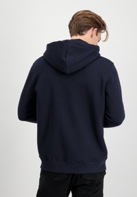 Hanorac cu glugă de culoare bleumarin, confecționat dintr-un material moale, cu un croi lejer, manșete și tiv cu nervuri, precum și un design clasic de buzunar tip kangur.
