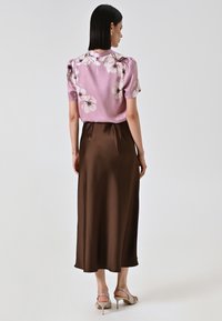 Zijden blouse in lichtroze met bloempatroon, gecombineerd met een bruine satijnen maxi rok. Korte mouwen met zachte plooien; over het geheel een gladde textuur.