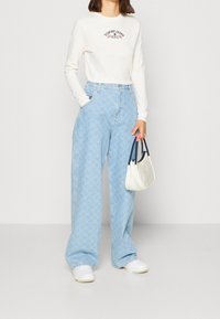 Světle modré džíny s širokým střihem a diamantovým vzorem, spárované s dlouhým rukávem off-white topem s vyšívanou značkou a malou bílou kabelkou.