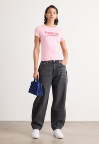 Pink short-sleeved T-shirt with "Tommy Jeans" logo, high-waisted black oversized jeans, white sneakers, and a small blue handbag.