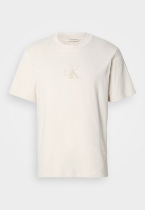 Kremasta pamučna majica kratkih rukava s izvezenim "CK" logotipom u svijetlosmeđoj niti. Klasični kroj s okruglim izrezom.