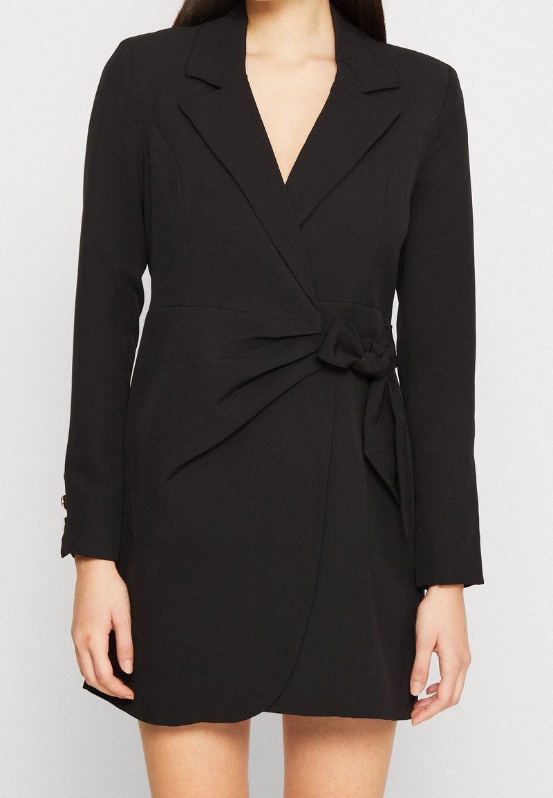 Vestido negro envolvente de tejido suave, con mangas largas, escote en V profundo y un detalle anudado en la cintura, con un corte ajustado.