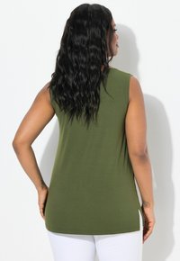 Olivově zelená, bezrukávová tunika s volným střihem. Má kulatý výstřih, boční rozparky a hladkou texturu látky. Bílý pozadí.