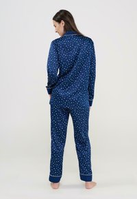 Conjunto de pijama azul marino de satén con patrones de estrellas blancas. Presenta mangas largas, puños en contraste y detalles decorativos en la costura.