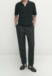 Polo shirt nero a righe con maniche corte e colletto a soffietto, abbinato a pantaloni neri larghi e sandali intrecciati neri.