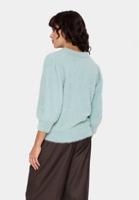 Light blue fluffy sweater with a round neckline and three-quarter sleeves, paired with dark brown wide-leg trousers. Soft texture, relaxed fit.
