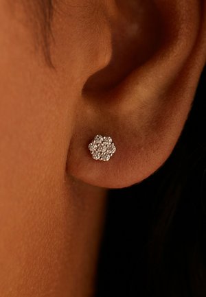 Clou d'oreille en forme de fleur en argent avec plusieurs petites pierres précieuses rondes et scintillantes. Gros plan montrant le lobe de l'oreille et la texture de la peau.