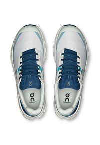 Baskets de sport blanches et bleues avec une tige respirante, surface texturée, semelle blanche épaisse et lacets bleus avec des accents de logo sur les côtés.