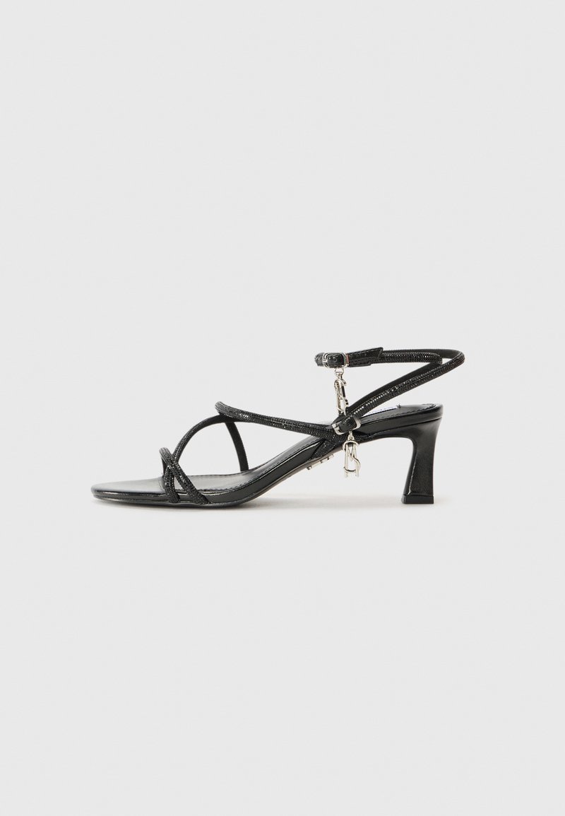 Sandales noires à talons avec de fines lanières, un petit talon bloc et un accent de charme métallique. Texture lisse et design minimaliste.