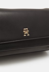 Bolso de mano de cuero negro con un acento de logo en tono dorado y un diseño estructurado, con una sutil textura y un detalle de costura limpio.