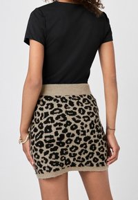 Haut noir à manches courtes associé à une jupe en tricot beige avec un motif léopard noir. La jupe a une taille côtelée.