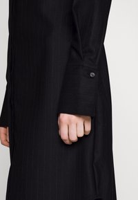 Svart randig kavaj med en jämn textur, utrustad med en knappmanchett och en skräddarsydd passform som betonar rena linjer och en strukturerad design.