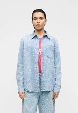 Hele sinine teksasärk peene leopardimustriga, nööbitav disain ja rinnatasku, kantud roosa graafilise T-särgi peal.