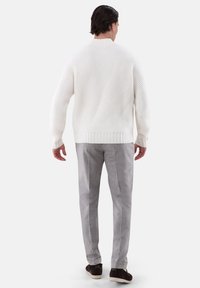 Weißer Strickpullover mit strukturiertem Muster, kombiniert mit hellgrauen Hosen und braunen Schuhen. Die Rückansicht zeigt gerippte Bündchen und Saum.