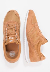 Esittelyssä New Balance 420 -tossut, joissa on hiekanvärinen mokkanahka- ja verkkopäällinen, valkoinen välipohja ja harmaat yksityiskohdat. Kengissä on pyöreä kärki ja nyöritys.