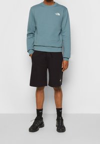 světle modrá mikina s kulatým výstřihem a logem, spárovaná s černými šortkami se bočními kapsami, nošená s černými teniskami a ponožkami.